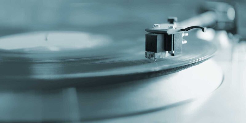 An LP record on a 1970's style turn table in black and white with a slightly blue hue